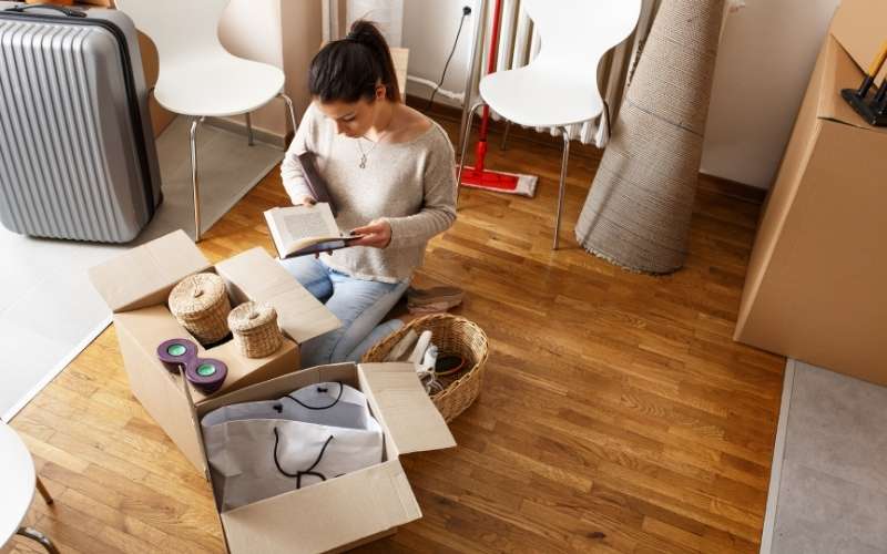 woman sitting in front of moving boxes holding a book and reading it