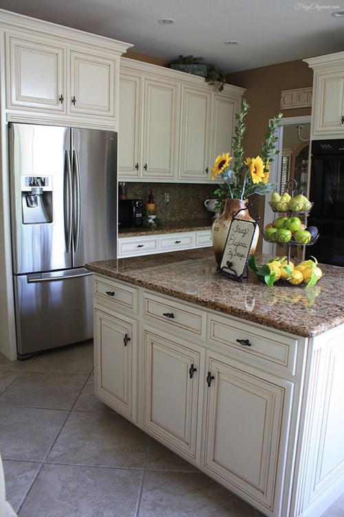 A kitchen island with cream cabinets and brown granite counters