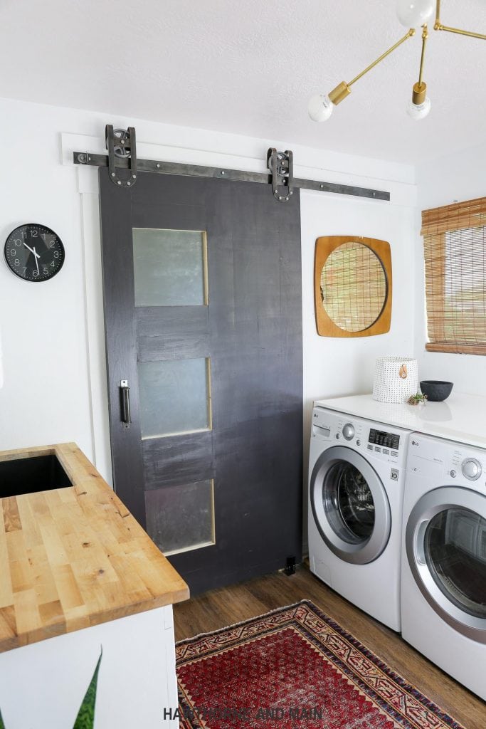 A laundry room with a black barn door and a red rug