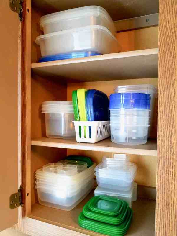 A kitchen cabinet with organized plastic food containers