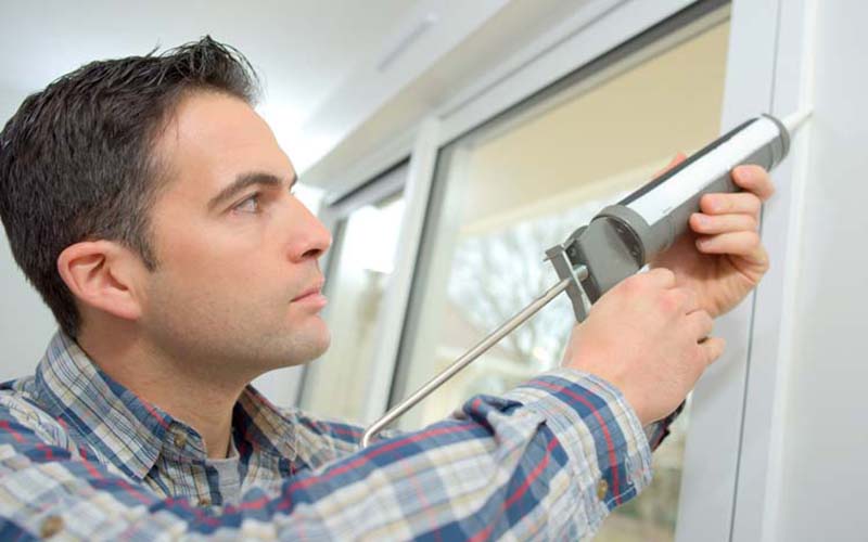 Man holding a caulking gun in a blog post titled can you caulk over caulk