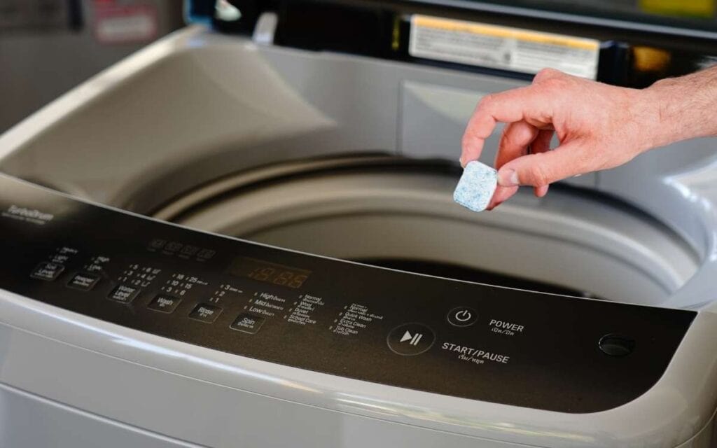 Hand of a man holding dishwashing cleaner over a washing machine