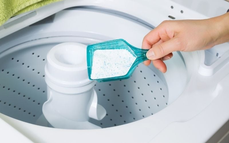 Pgoto of a hand holding a scoop of dishwashing detergent over a washing machine