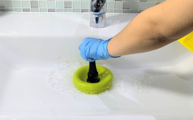 Photo of a hand with blue gloves holding a plunger over the drain of a sink