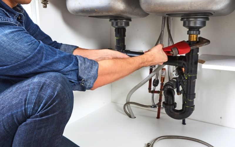 image of a plumber holding a wrench fixing the drain under the sink