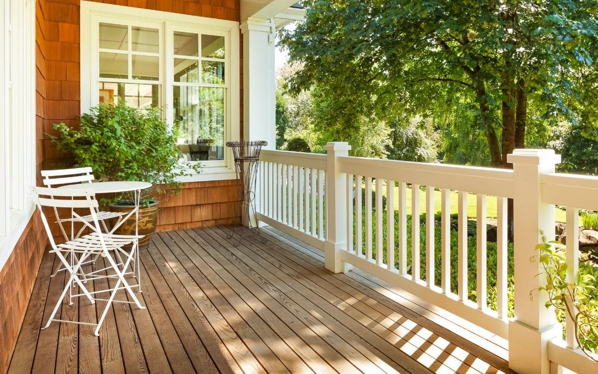 Photo of a clean porch with white railings, a plant in large pot and a tree nearby