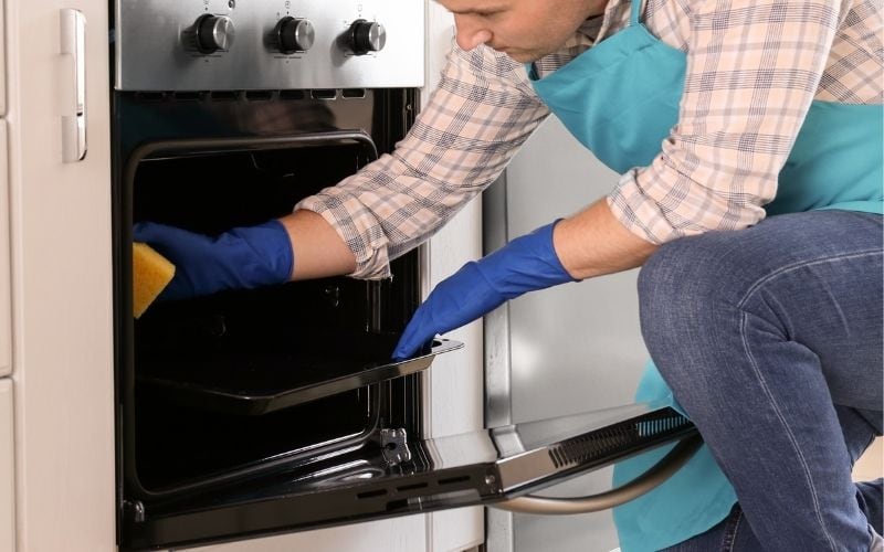 Photo of a man wearing gloves and cleaning the inside of oven
