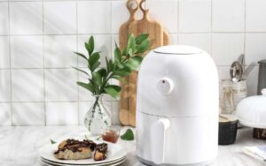 Pho to white air fryer beside a plate and wooden chopping board on counter top