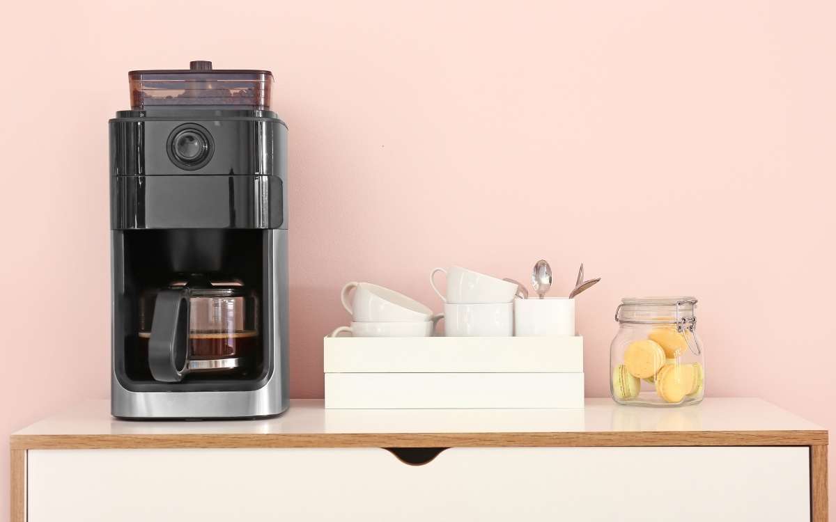 Photo of coffee maker with cups on a tray and a jar with cookies on a small table