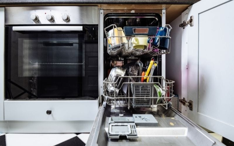 Imaage of an opened dishwasher with dishes inside beside an oven