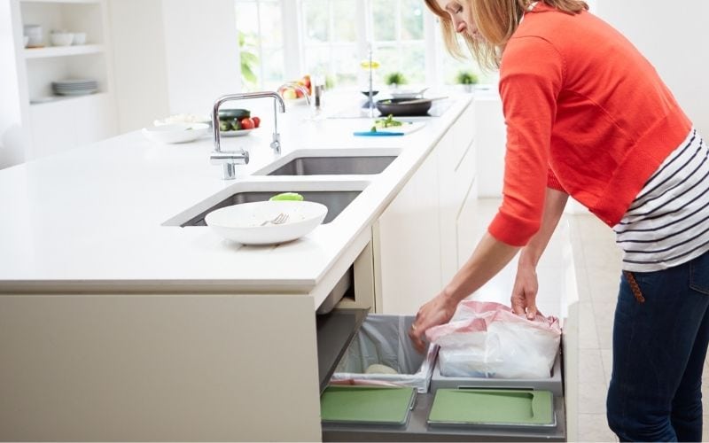 Photo of a woman looking at the pull out trash can in the kitchen