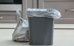 Photo of a grey colored trash bin and a tied garbage plastic bag on the floor
