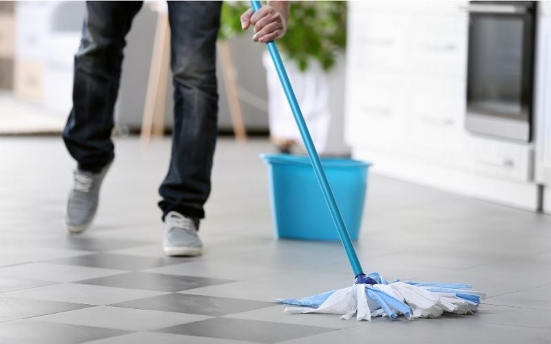 Photo showing a person mopping the floor with a bucket nearby