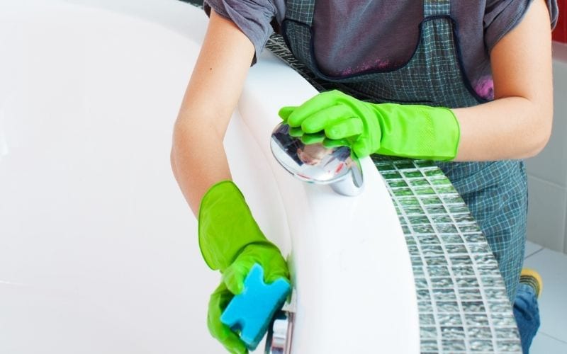Photo of a person with gloved hands while cleaning a bathtub