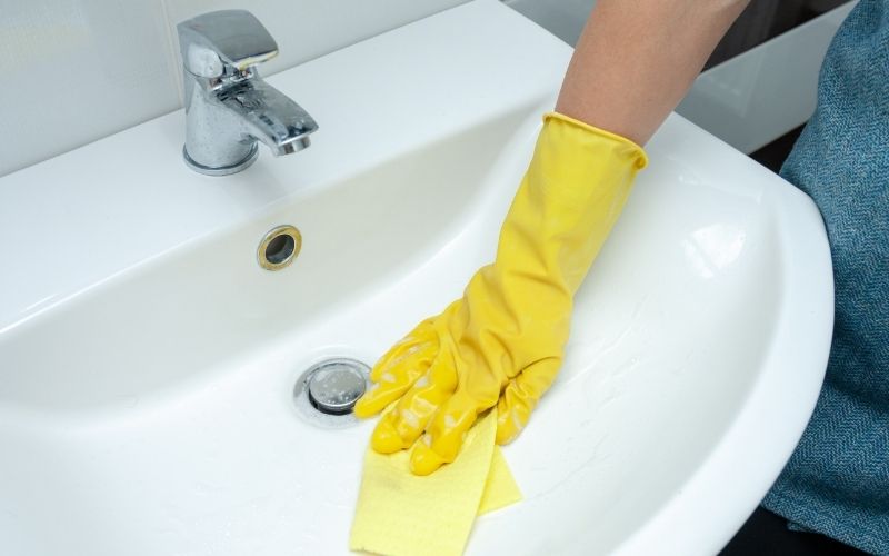 Photo showing a gloved hand with a rag cleaning the sink