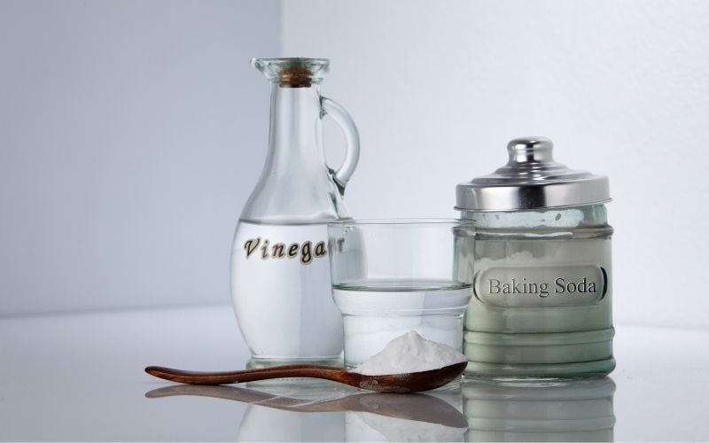 Image showing a bottle of vinegar, a jar of baking soda, a glass of water and a spoon with white powder on a counter top