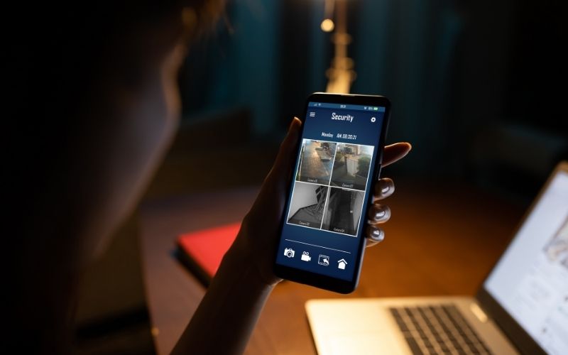 Photo showing a hand holding a smart phone that shows images of different rooms