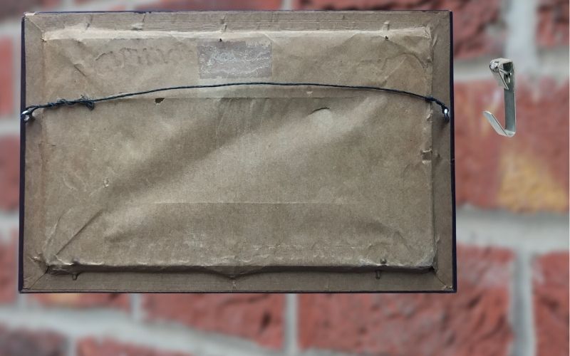 Image of the back of the frame with wire beside a hook with blurred brick background