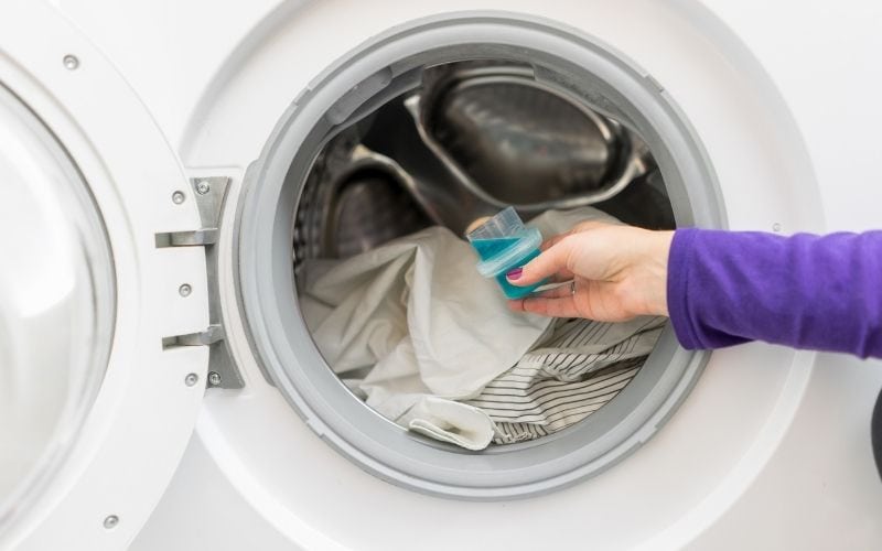 Photo of clothes in washing machine with a hand holding a cup with liquid