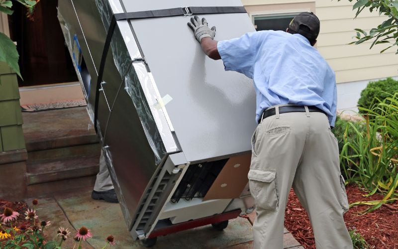 Two person carrying a fridge into the house