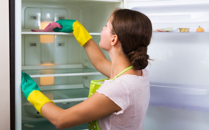 Woman with gloves on her hands while cleaning the inside of the fridne