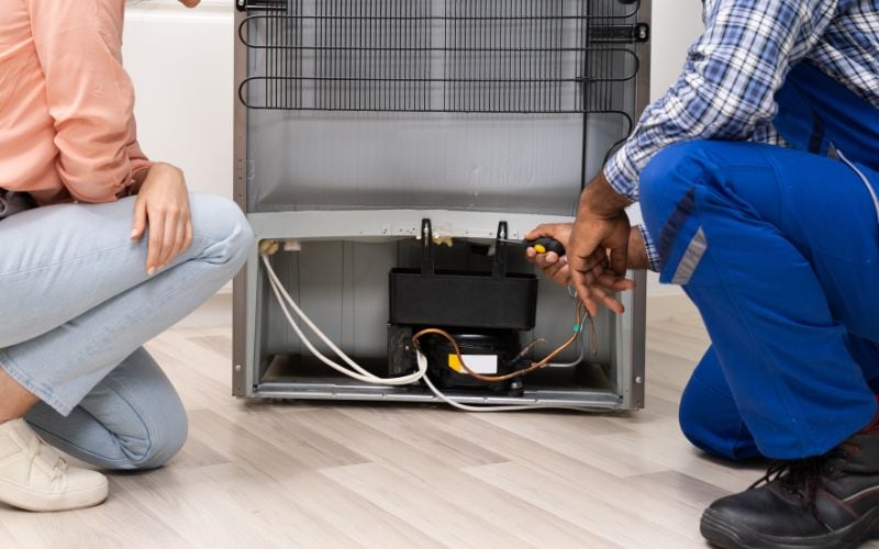 Two people at the back of a refrigerator and checking the lower part.