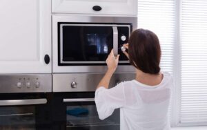 A woman turning the knob of a microwave oven placed in a cabinet