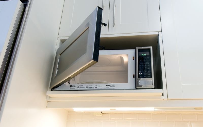 A microwave oven inside a cabinet with a light underneath the cabinet