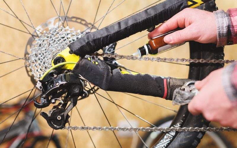 A hand holding a bottle of oil while squeezing it out into the chain of the bike