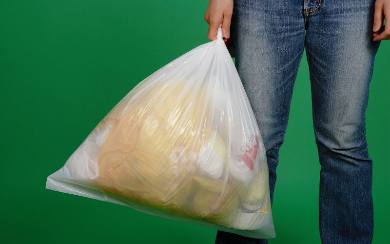 A person carrying a white plastic bag with trash where maggots can be in it in green background