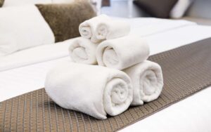 Rolled white towels placed on a bed that looks like inside a room of a hotel