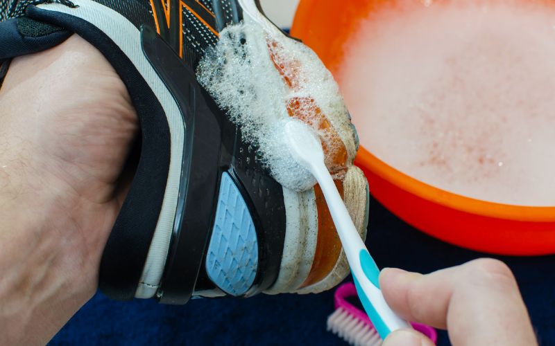 a hand with a toothbrush being used to clean a shoe