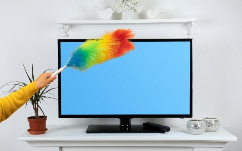 A hand holding a duster cleaning a flat screen tv.
