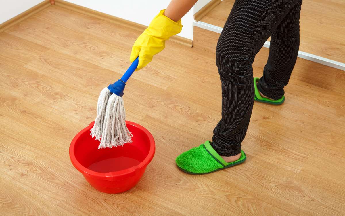 A person holding a mop over a red basin